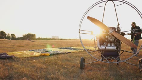el parapente motorizado está en el campo al atardecer con una hélice de madera, y el piloto extiende el paracaídas y alinea las eslingas