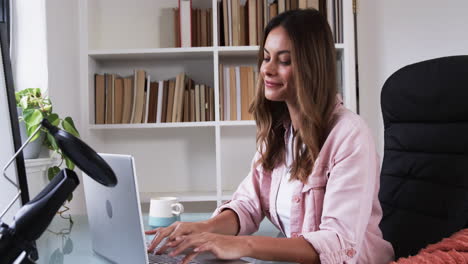 smiling woman working on laptop at home office with books and coffee