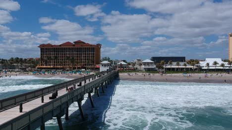 Aerial-shot-following-waves-breaking-on-the-shoreline-next-to-a-pier