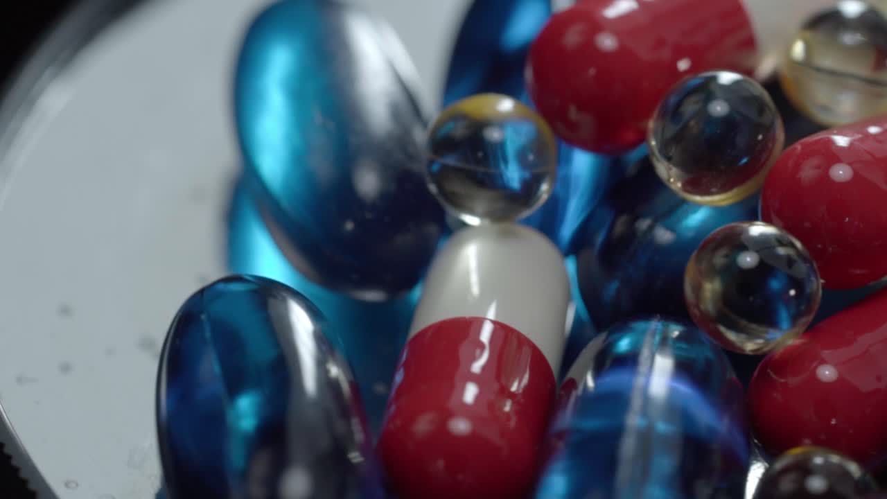 Close up of assorted capsules and gel pills placed together on reflective surface, studio lighting