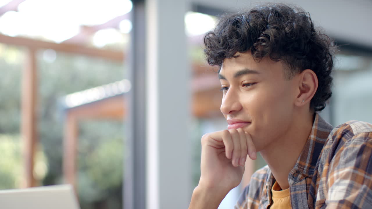 Smiling young man with curly hair sitting indoors, looking thoughtful, copy space