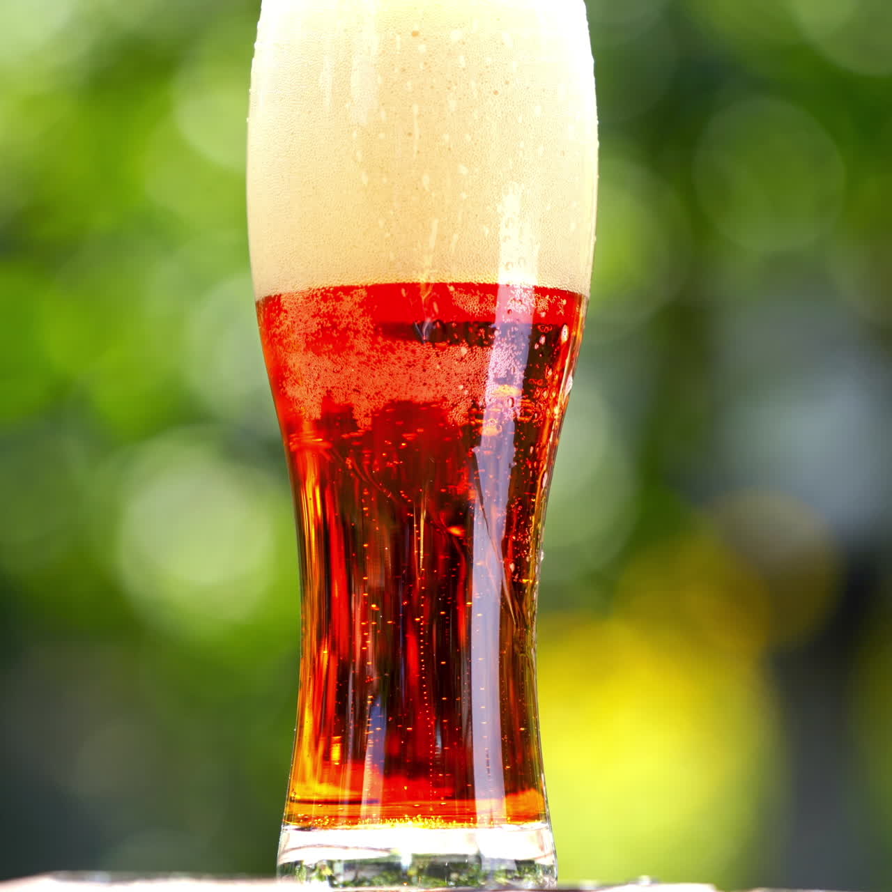 White foam becoming into dark beer with bubbles in glass. Foamy alcohol beverage in a tall glass on blur background. Close-up.