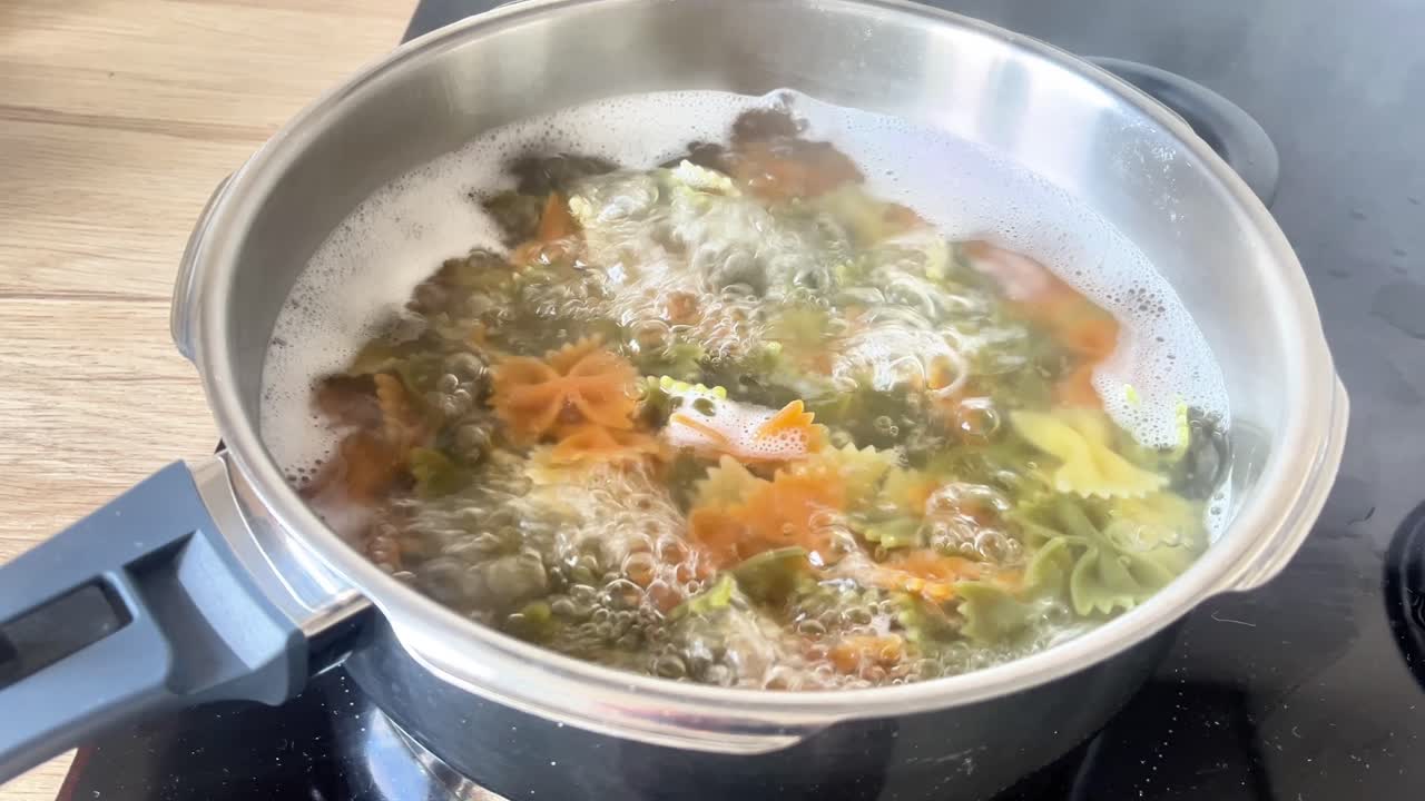 Una olla de comida está hirviendo en una estufa. La comida es una mezcla de verduras y pasta.