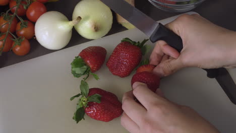 woman's hand and sharp knife cutting the red strawberry on the chopping board. - close up shot