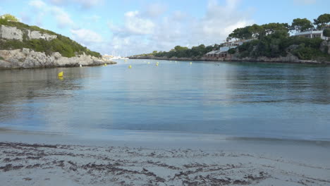 large view at early morning of the beach at creek cala santandria in menorca with yellow boat markers, blue sea and surrounding rocks