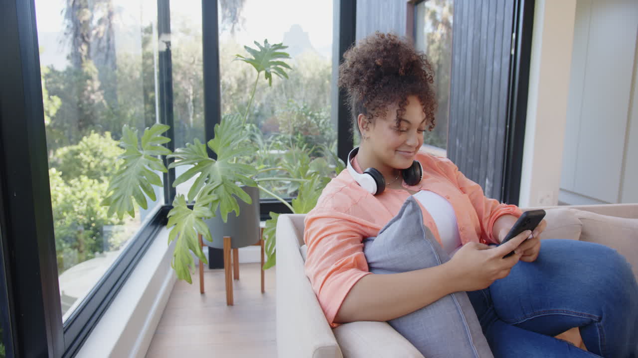 Relaxing on couch, woman with headphones using smartphone in bright living room