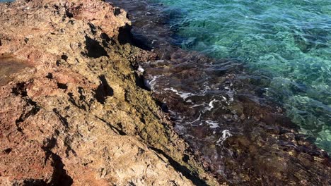 waves gently washing over rugged coastal rocks with clear blue water in crete, greece