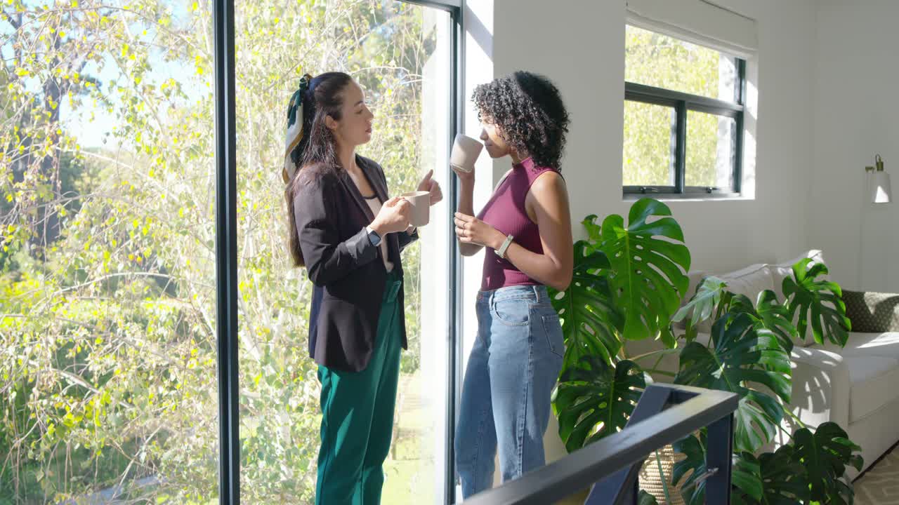 Female friends maintaining eye contact and starting conversation, gesturing, sipping mugs by window