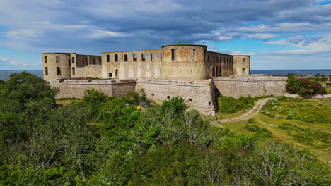 Vista-Panorámica-De-Las-Ruinas-Del-Castillo-De-Borgholm-Enclavadas-En-Un-Exuberante-Campo-Verde-Bajo-Un-Cielo-Azul-Nublado-En-Borgholm,-Öland,-Suecia---Amplia-Panorámica-A-La-Izquierda