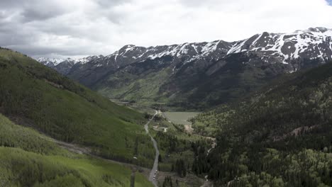 Colorado-Rocky-Mountains-with-snowed-peaks-and-small-lake-below,-Aerial-flyover-shot