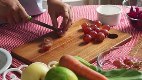 woman hands cutting red grapes on wooden board with knife in preparation making healthy diet food