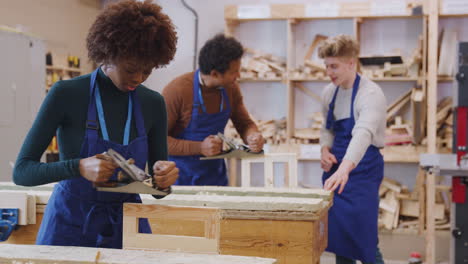 tutor with carpentry student in workshop studying for apprenticeship at college using wood plane