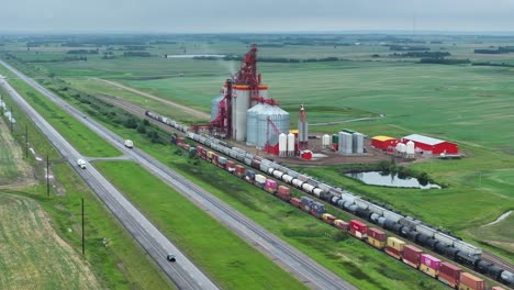 Eine-Luftdrohnenaufnahme-Eines-Güterzuges,-Der-An-Einem-Modernen-Getreidesilo-In-Der-Prärie-Von-Saskatchewan-Vorbeifährt