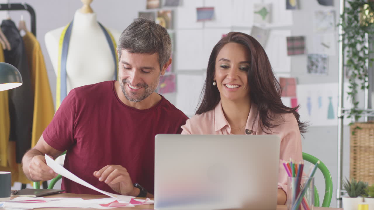 diseñadores de moda masculinos y femeninos en el estudio haciendo llamadas de video y mostrando diseños en el escritorio en la computadora portátil