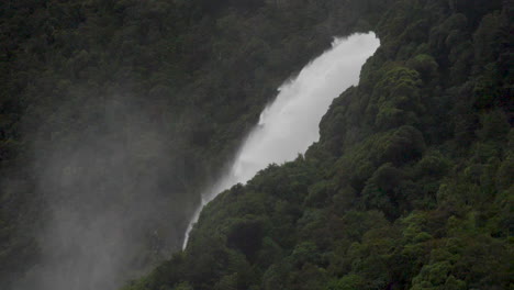 slow motion shot of a large waterfall in milford sound after a rain storm with mist - piopiotahi, new zealand