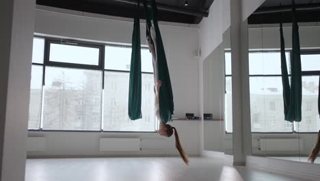 a young beautiful woman performs exercises on a hammock from aero yoga. a woman in the afternoon in front of the mirror in the hall performs stretching alone