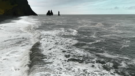 wide foamy white waves arrive to the beach with black volcanic sand. drone flight above the raging waterscape of the north atlantic ocean.