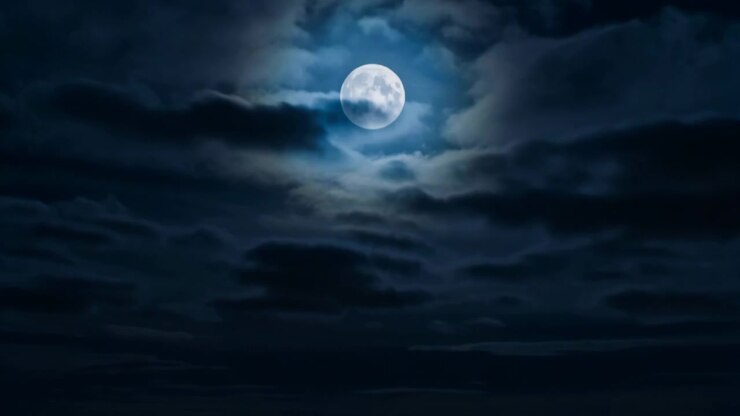 Una luna piena luminosa con un alone morbido pende sopra nuvole scure a strati, mentre la griglia urbana estesa, le autostrade e i lampioni brillano sotto in una suggestiva luce urbana notturna e un profondo contrasto, con luna, notte.