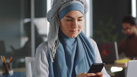 businesswoman in hijab using smartphone and posing for camera