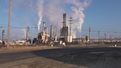 greenhouse smoke raising from an oil refinery on a muddy road under a blue sky