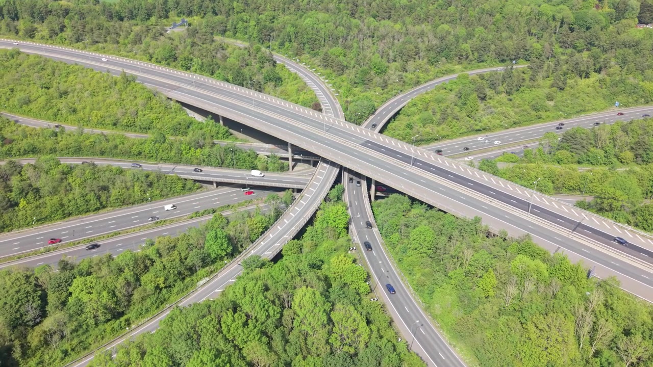 An aerial view shows a large motorway interchange with cars and trucks driving on multiple levels of roads.
