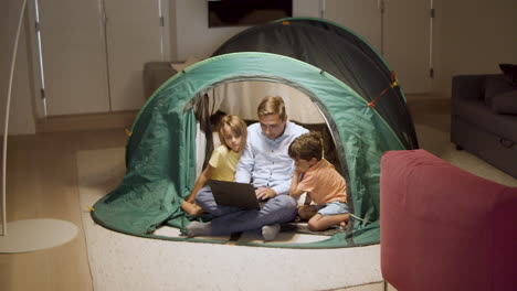 dad and children watching horror movie on laptop in tent