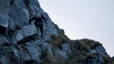 excursionista sube grandes rocas bajo un acantilado al atardecer