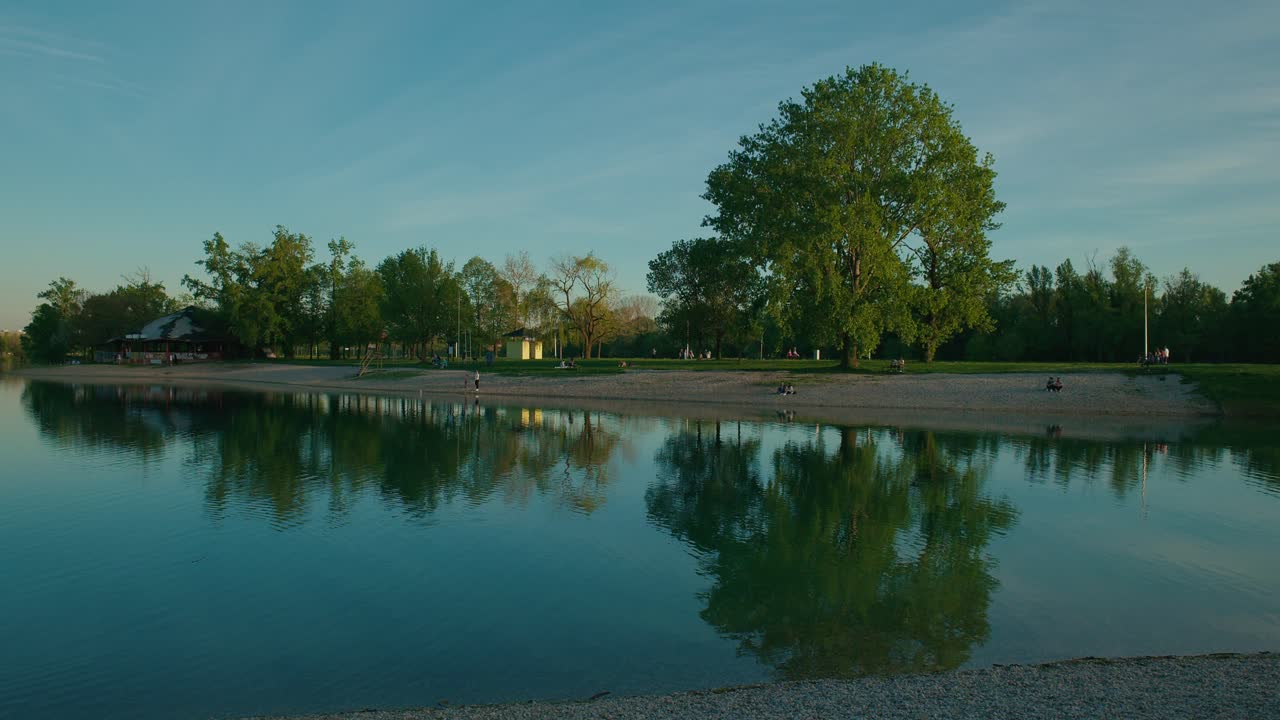 Lago sereno con riflessi nitidi, vegetazione lussureggiante e una riva sabbiosa al tramonto nel Lago Jarun, Zagabria Croazia.