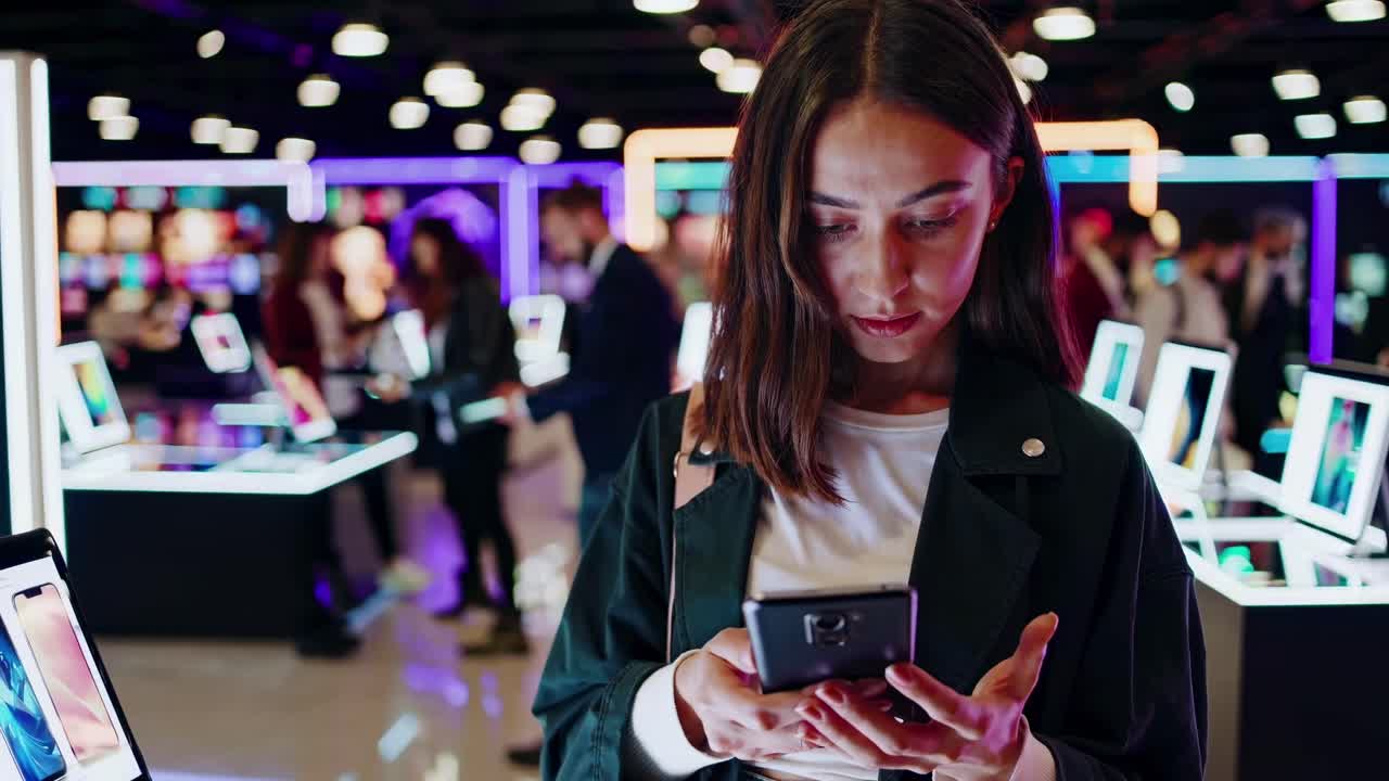 A woman uses her phone in a tech store, surrounded by glowing screens