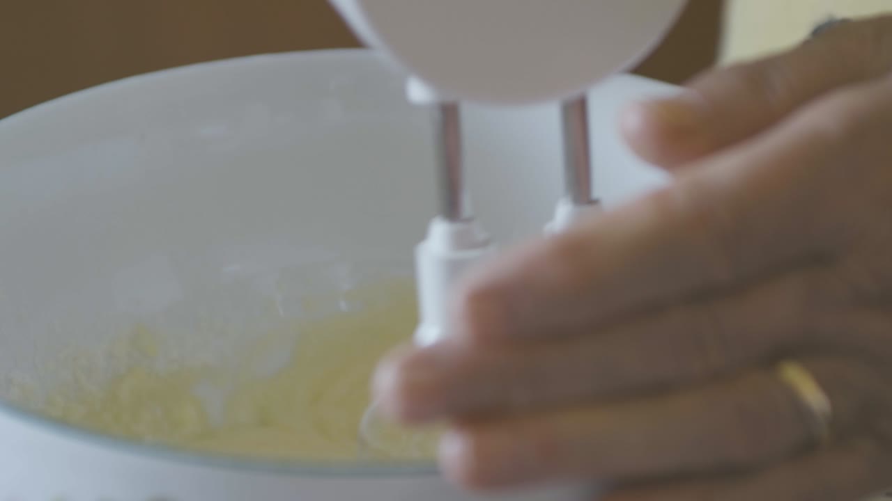 una dama mezcla huevos y azúcar para hacer ponche de huevo, su mano lleva un anillo de bodas