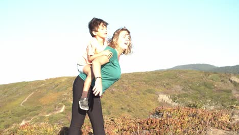 Active-mom-piggybacking-kid,-walking-on-mountain-path