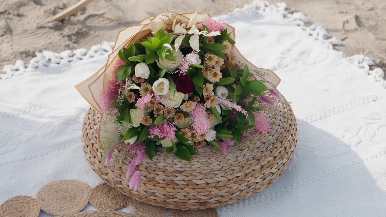 colorful wedding bouquet placed on straw pouf atop white blanket on sandy beach