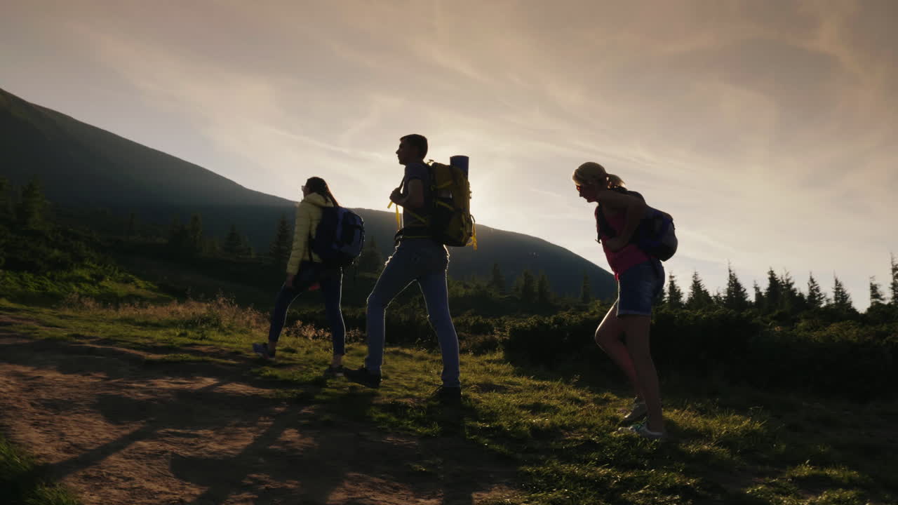 배낭을 메고 있는 한 무리의 친구들이 석양의 광선을 받으며 산을 올라간다
