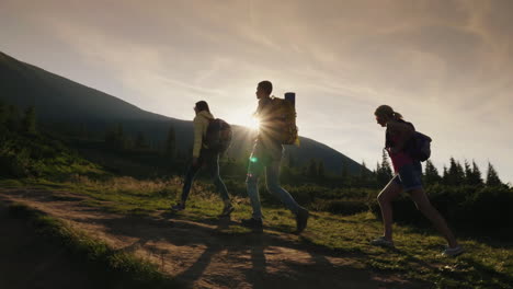 a group of friends with backpacks rises up the mountain in the rays of the setting sun active lifest