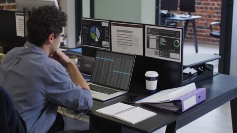 caucasian man sitting at desk watching coding data processing on laptop and computer screen