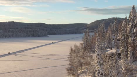 Beautiful-winter-scenery-with-skiers-on-a-frozen-lake,-aerial-view-with-trees-nearby,-and-mountains-in-the-background