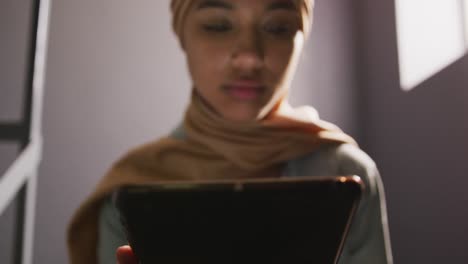 estudiante asiática vestida con un hijab beige sentada en las escaleras y usando una tableta