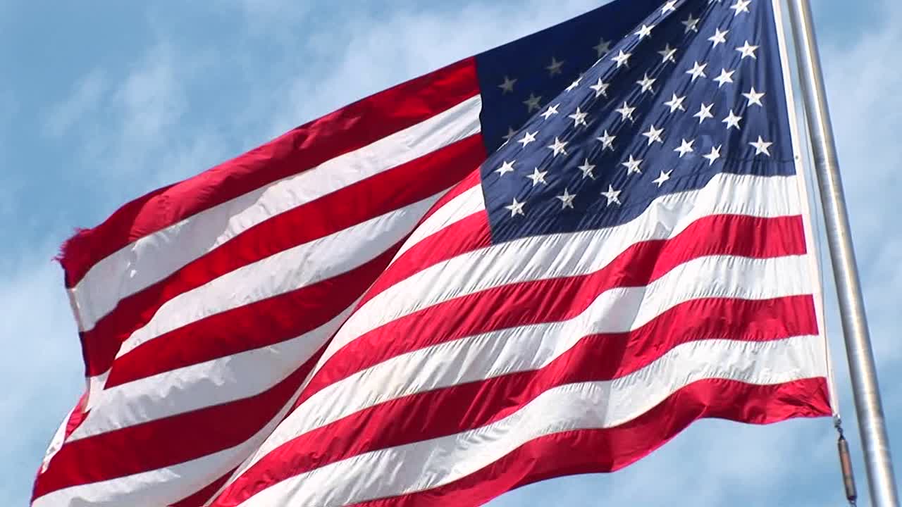 la cámara gira a la derecha a través de una ondulante bandera estadounidense que revela la estatua de la libertad en el fondo