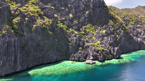 jagged limestone cliffs covered in greenery tower above vibrant turquoise waters along the northern coast of talisay beach on tapiutan island in the philippines under a clear sunny sky