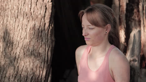 una mujer joven está sentada debajo de un árbol y mira a su alrededor mientras el rayo del sol cae sobre su rostro