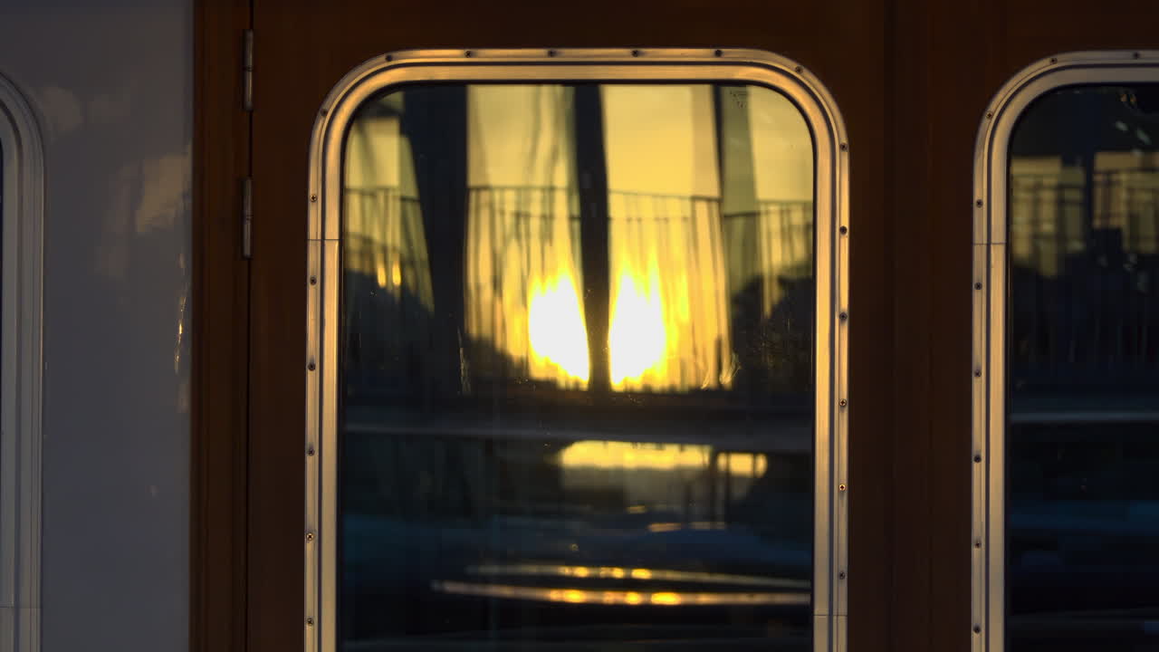 Close-up of a yacht's window reflecting the golden sunset and marina railings in Cannes