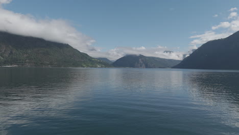 slowmotion drone shot coming close to the water towards the fjords in norway on a sunny and cloudy day with mountains and green in the background and reflecting water log