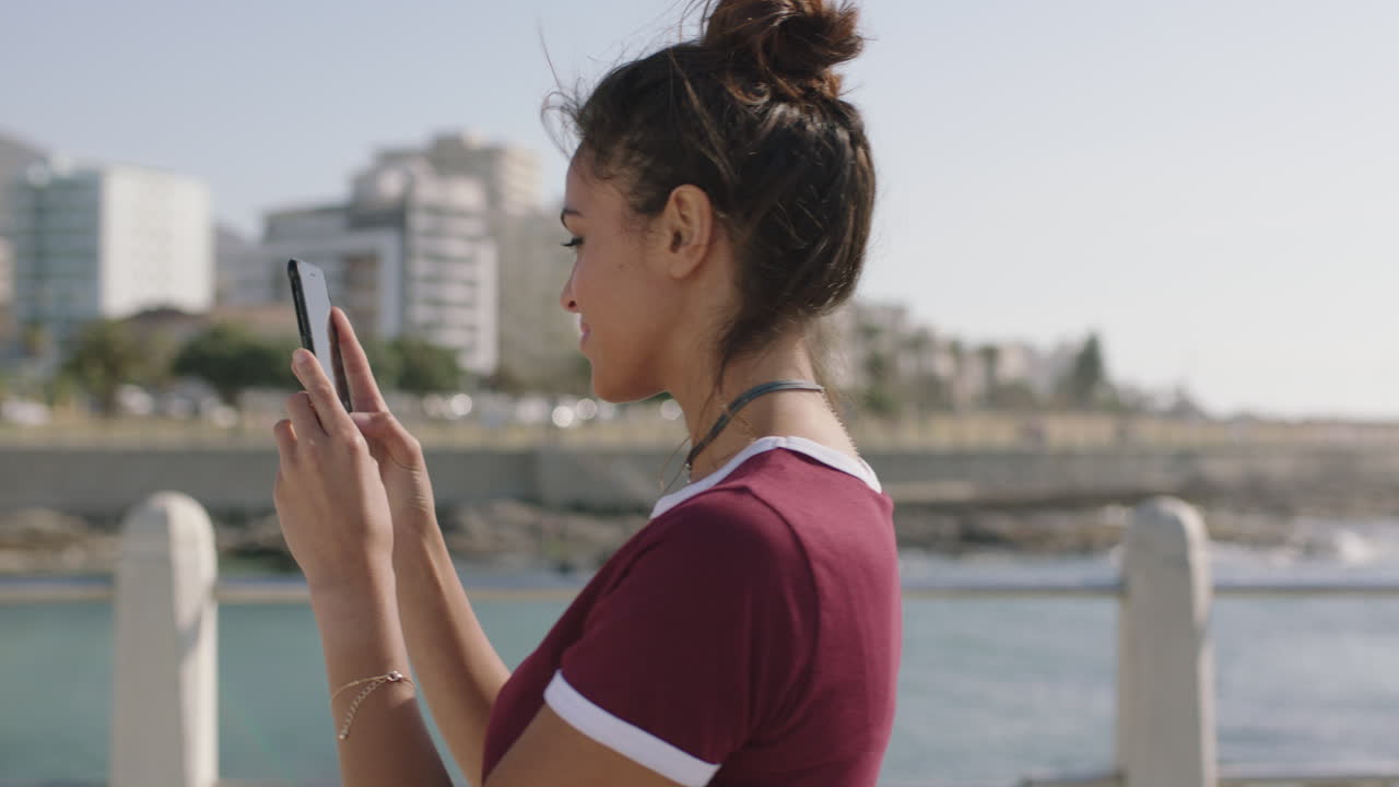 retrato de una joven hermosa mujer hispana usando un teléfono inteligente tomando fotos en una hermosa playa soleada