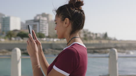 Porträt-Einer-Jungen-Schönen-Hispanischen-Frau,-Die-Mit-Ihrem-Smartphone-Ein-Foto-Am-Wunderschönen-Sonnigen-Strand-Macht