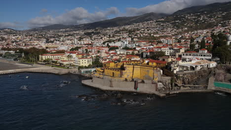 aerial shot in distance of the madeira fort in the city of funcal and where the houses and buildings of the coast can be seen