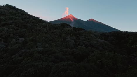 passing close to tree tops towards sunlit peak of smoking volcano, aerial fpv view