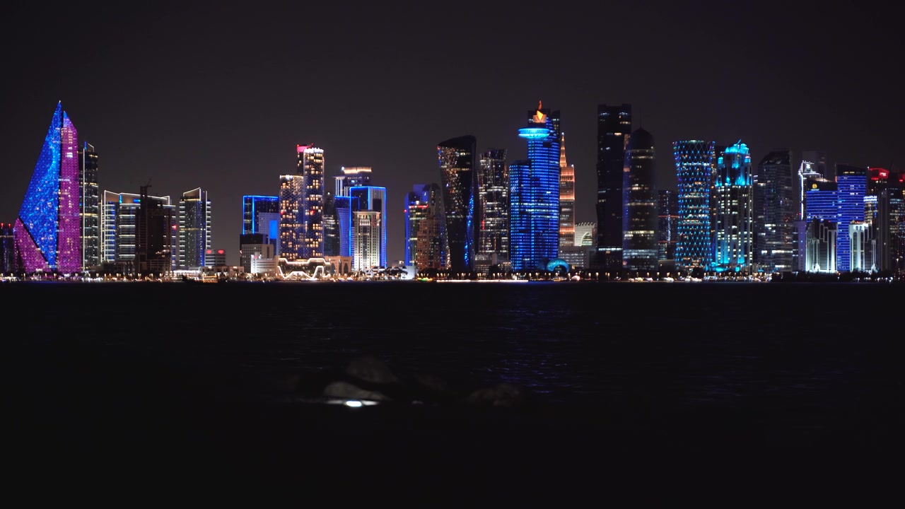 Fantastisk nattlig bybilde av Doha, Qatar. Byens ikoniske futuristiske tårn gløder i levende blå og lilla nyanser, som reflekteres perfekt på den rolige Persiabukta