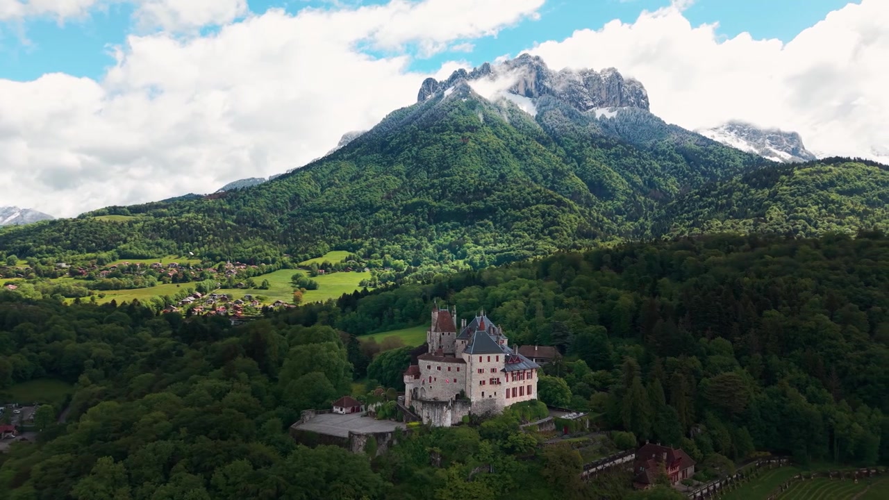 Ripresa aerea intorno al Castello di Menthon Saint Bernard nel dipartimento dell'Alta Savoia, vicino al Lago di Annecy, con la montagna Dents de Lanfon sullo sfondo, regione Alvernia-Rodano-Alpi, Francia