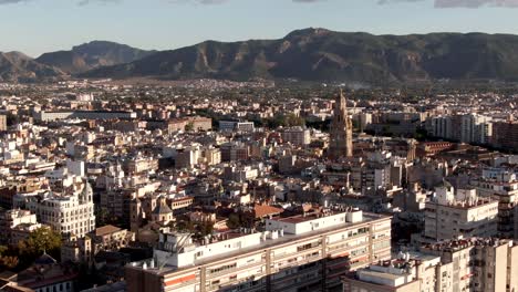 Toma-Aérea-Sobrevolando-La-Ciudad-De-Murcia-Con-Un-Fondo-De-Montaña-En-España