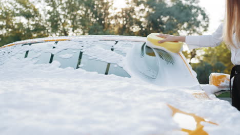 woman washing a yellow car with a sponge